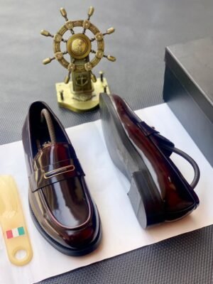 A pair of shiny black leather loafers on a white paper with a shoe horn and a decorative ship wheel in the background, showcasing premium products in Nigeria at Tconcorde.